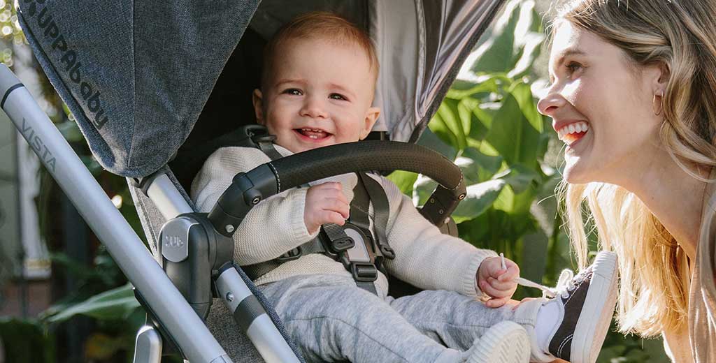Happy smiling baby in an Uppababy stroller, with mom nearby.