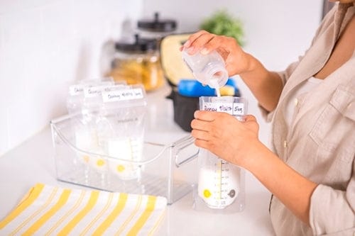 Woman holding Medela breast milk storage bag and filling with expressed milk from bottle.