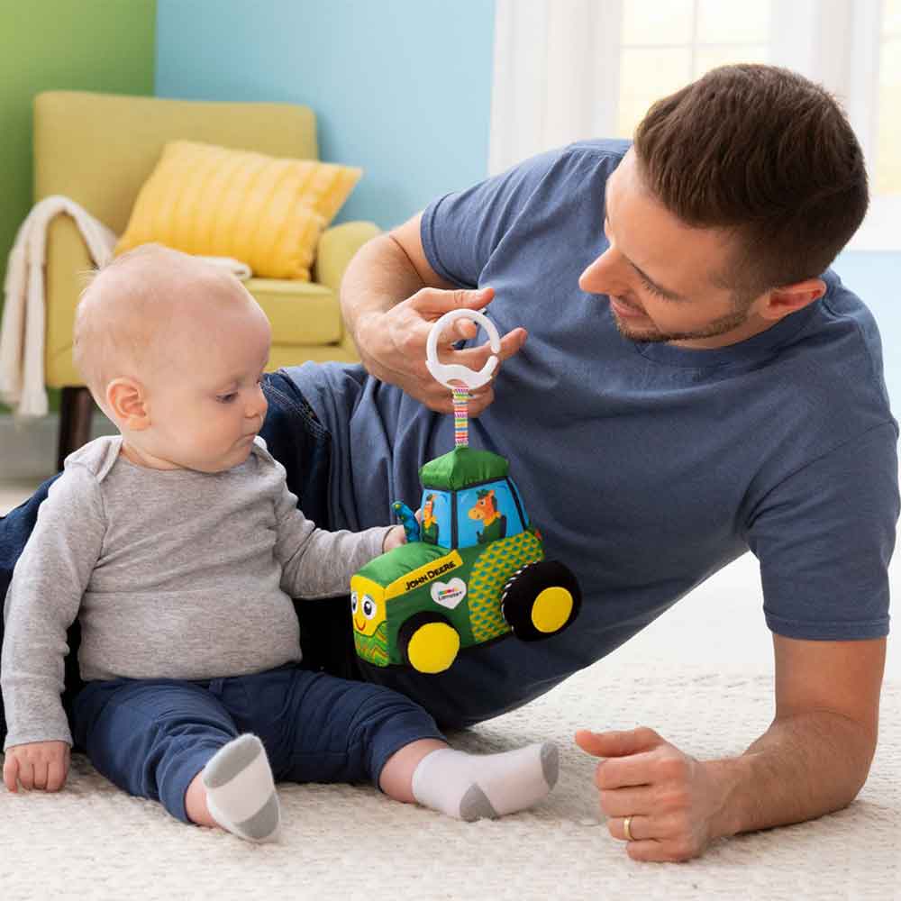 A father trying to interact with his son with the John Deer Clip & Go Tractor by Lamaze.