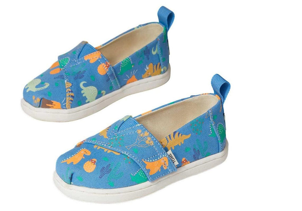 Tiny Toms slip on with velcro on azure blue with a dino pattern in orange and green. The shoes are glow in the dark
